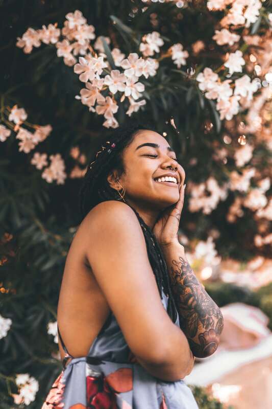Young woman smiling under a tree with flowers. This illustrates the a person who has healed thier childhood trauma through online therapy in Kansas with Sacred Circle Holistic Healing.