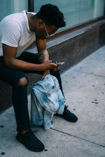 Young Black man looking at this iPhone. This represents that Sacred Circle Holistic Healing helps young people learn to set healthy boundaries.