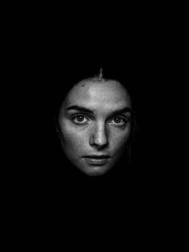Black and white picture of a young woman's face illuminated by light, surrounded by darkness. This illustrates how inner child healing work can felt scary and intimidating.