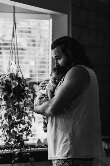 the side profile of a father holding his baby in black and white. This represents that Sacred Circle Holistic Healing offers online grief counseling in Kansas for bereaved parents.
