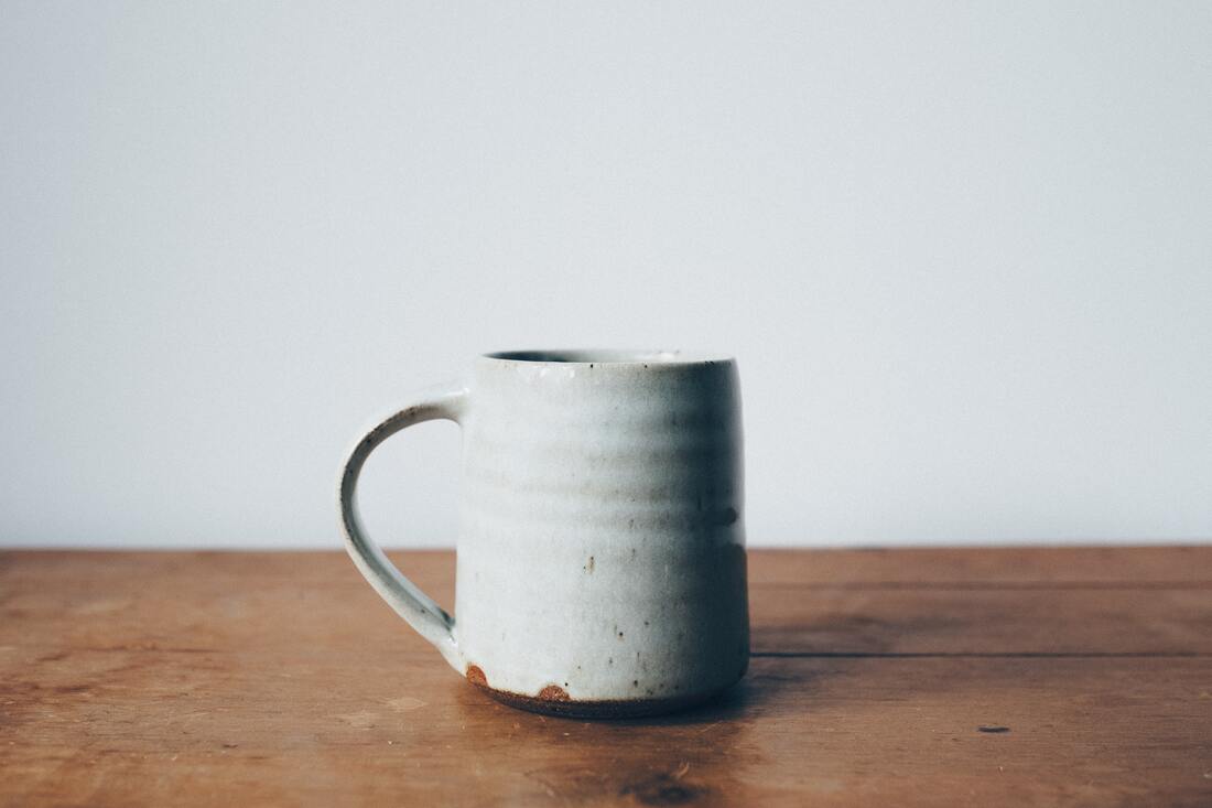 White, rustic mug sitting on a wooden table in front of a white wall. This illustrates that Sacred Circle Holistic Healing offers online therapy to help young adults learn about boundaries, self-compassion, and mindfulness, all of which protect against the effects of toxic relationships. 
