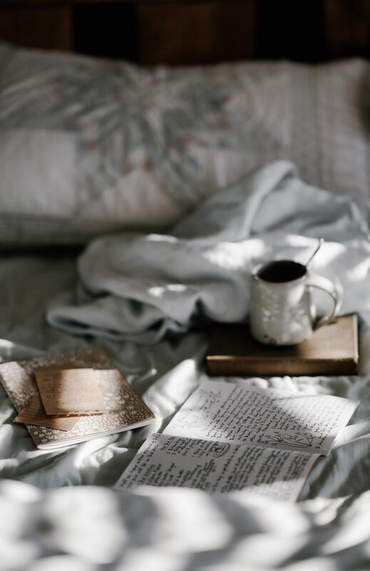 A open journal and notebooks lying one a bed with a mug. This illustrates the importance of self-care and that Sacred Circle Holistic Healing offers online therapy in Kansas to help people heal inner child wounds.