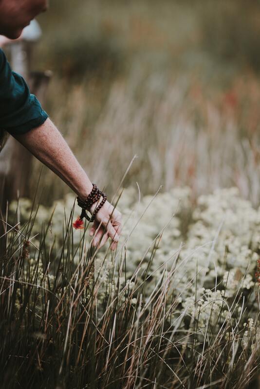 Woman wearing prayer beads touching wild flowers. This represents that narcissistic abuse can happen to anyone. Sacred Circle Holistic Healing offers online therapy in Kansas for toxic relationships and narcissistic abuse. 