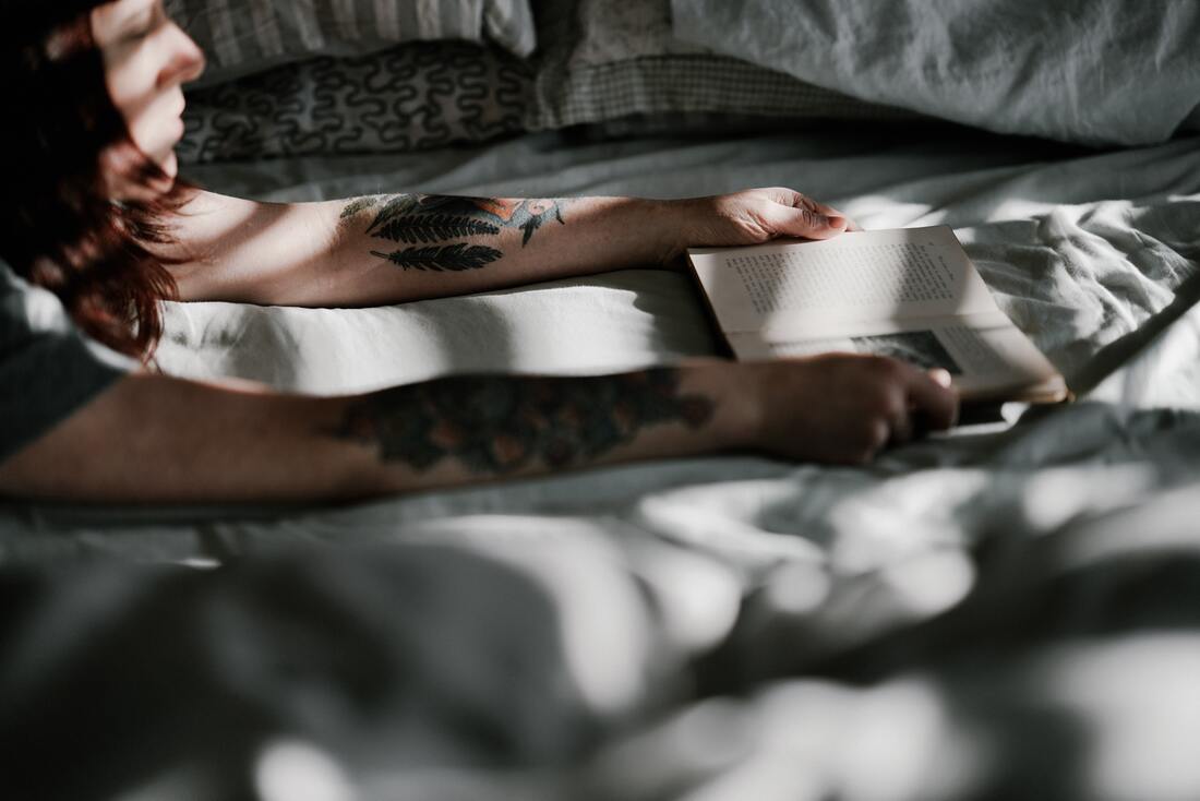 Young woman lying on the bed looking at a book. This illustrates the importance of self-reflection and self-awareness in mental health.