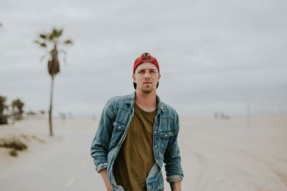 Young man in red hat and denim shirt standing on a beach, facing the camera. This represents that Sacred Circle Holistic Healing provides holistic therapy for adults in Lawrence, KS 66045