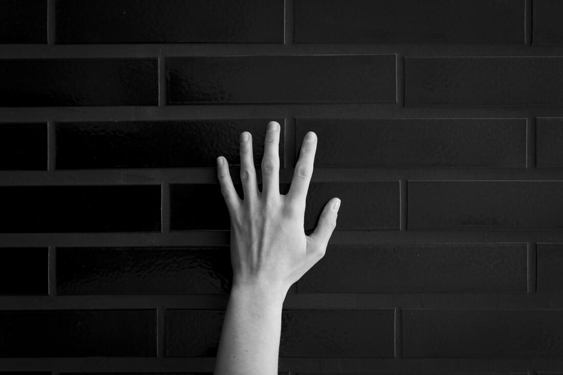 Black and white photo of a hand in front of bricks. This represents the starkness of the pain of narcissistic abuse. Sacred Circle Holistic Healing offers counseling for toxic relationships throughout Kansas.