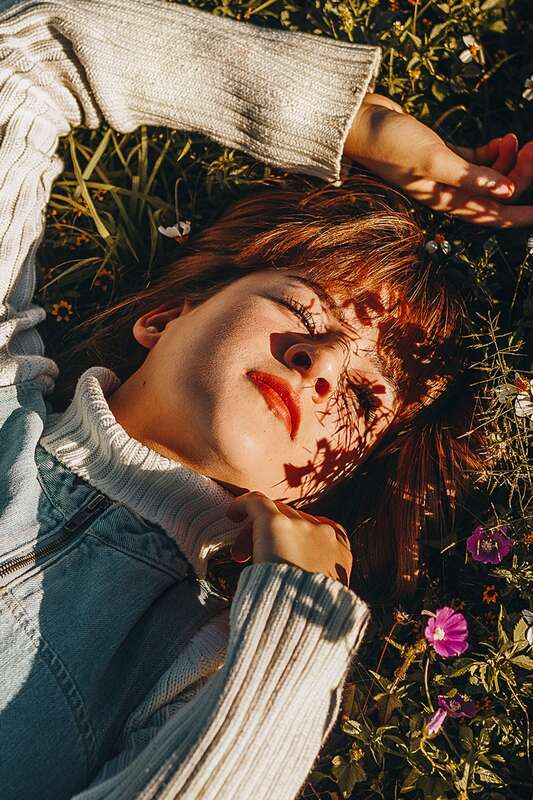 Young woman lying in the grass looking into the sunlight. This illustrates how Highly Sensitive People process deeply and feel emotions deeply.