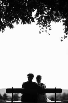 black and white silhouette of a woman and man sitting on a bench. This illustrates how grief can feel lonely. Sacred Circe Holistic Healing offers online grief counseling in Kansas.