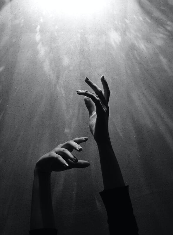 Black and white photo of hands reaching up toward the light. This represents how grief can feel dark, and how our being embodied can help us cope with grief. Sacred Circle Holistic Healing offers online grief and bereavement counseling throughout the state of Kansas.