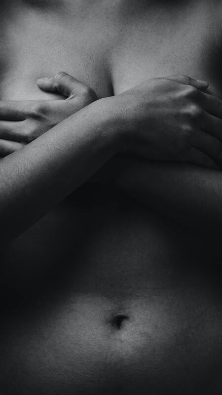 Close up of woman's naked torso in black and white, hands over her breasts. This illustrates that Sacred Circle Holistic Healing offers online counseling to young women who struggle with anxiety and low self-esteem.