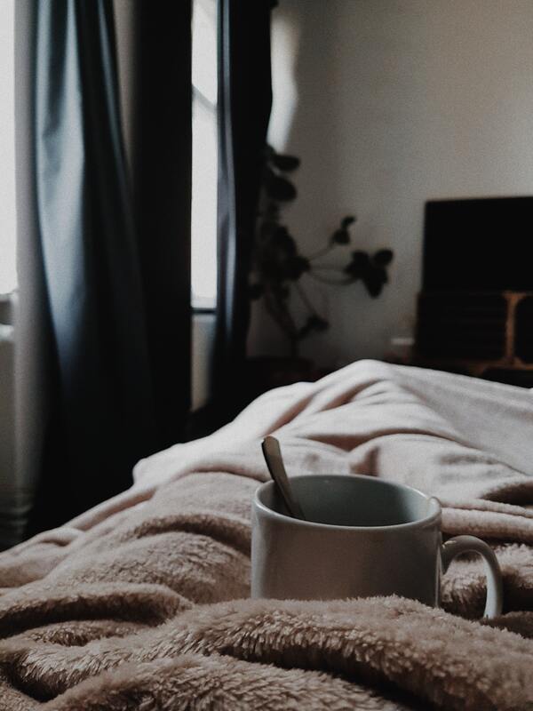Photo of ceramic mug sitting on cozy blankets. This illustrates that self-care is essential, and that Sacred Circle Holistic Healing helps young adults learn how to have self-compassion through online therapy in Kansas.