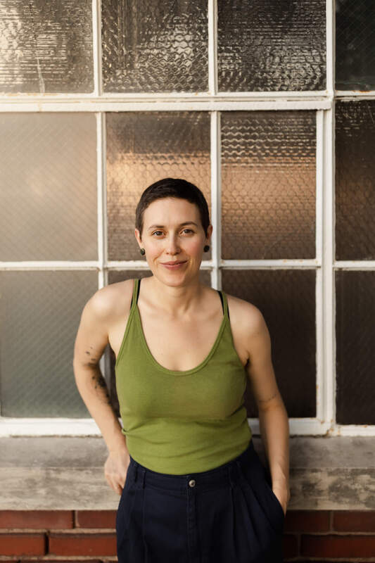 Picture of Maggie Jones Boyle, Licensed Professional Counselor standing in front of a window wearing a green tanktop and navy blue pants. 