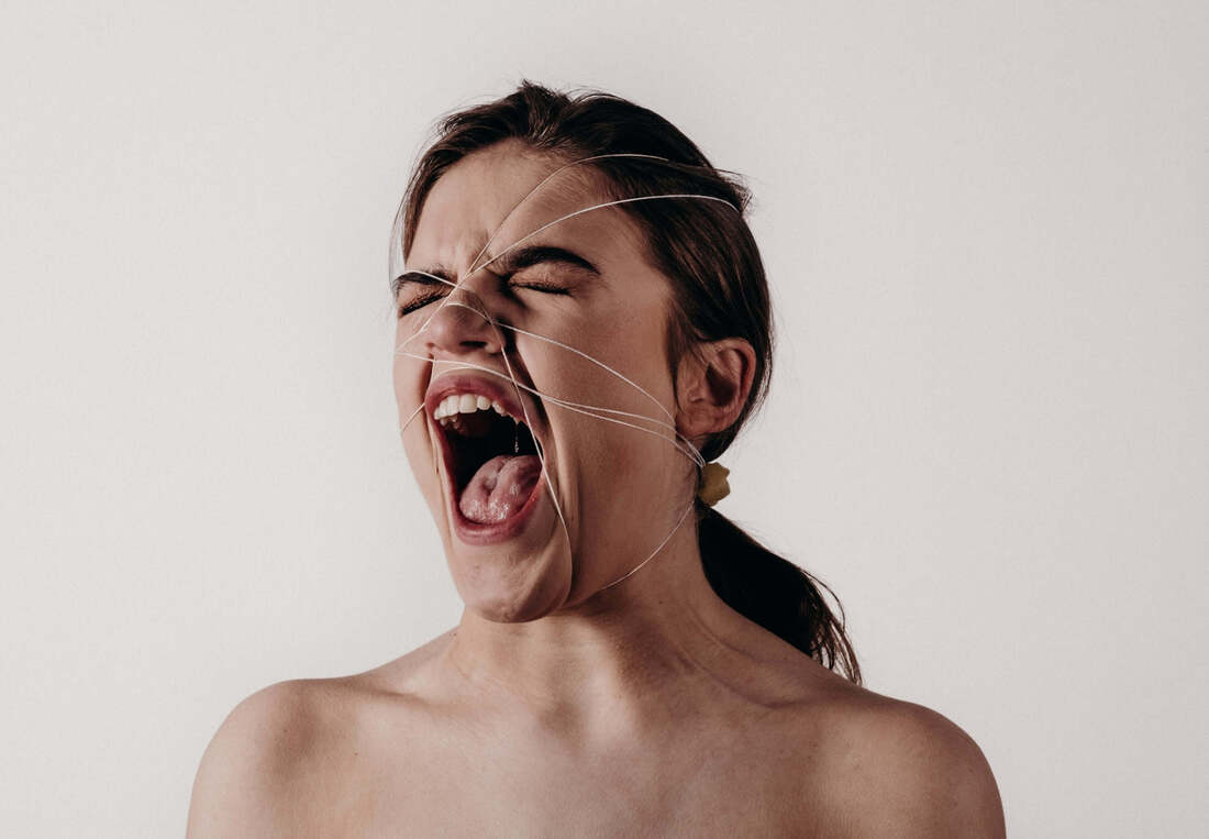 White woman screaming, eyes closed with a string wrapped over her face. This illustrates how trapped we can feel in our emotions and how therapy with Maggie Jones Boyle, therapist based in Lawerence, Kansas can help.
