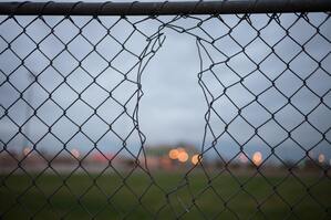 Chain-linked fence with a hole in it. This represents an unhealthy boundary. Sacred Circle Holistic Healing offers online counseling in Kansas for women working on their boundaries.