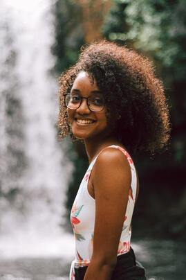 Young Black woman smiling into the camera. This illustrates that Sacred Circle Holistic Healing offers online therapy in Kansas for young woman struggling with low self-esteem and anxiety.