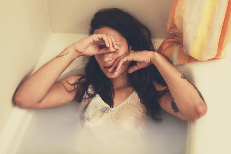 Woman clothed in bathtub, hiding hiding her face. This represents that Sacred Circle Holistic Healing offers counseling to women with low self-esteem and childhood trauma.