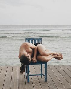 Photo of white man with long hair in underwear lying on his side, curled up, on a chair in front of the ocean. This illustrates that Sacred Circle Holistic Healing offers online counseling in Kansas for Highly Sensitive People.