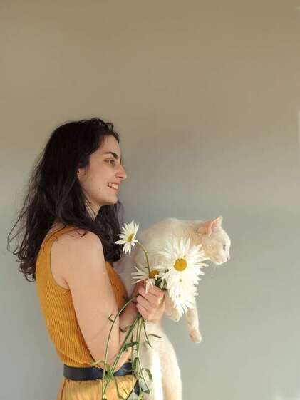 Young woman smiling, holding a white cat and flowers repesenting the young adult clients who come to Maggie Jones Boyle for holistic therapy in Lawrence, Kansas. 