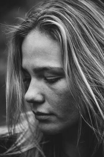 Black and white portrait of a young woman looking down, off camera, not smiling. This symbolizes that Sacred Circle Holistic Healing offers online grief and bereavement counseling in Kansas.