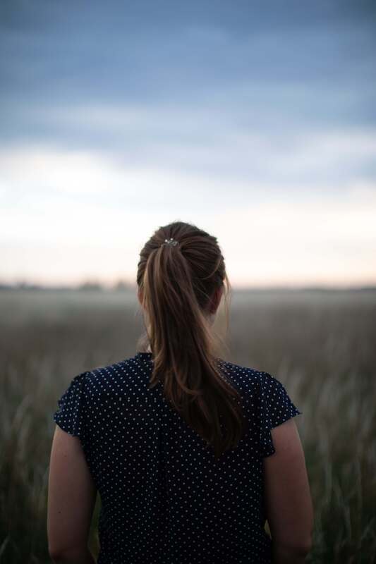 The back of a woman standing in a field. This illustrates the feelings of the adults who come to therapy to heal their anxiety and low self-worth online in Kansas. 