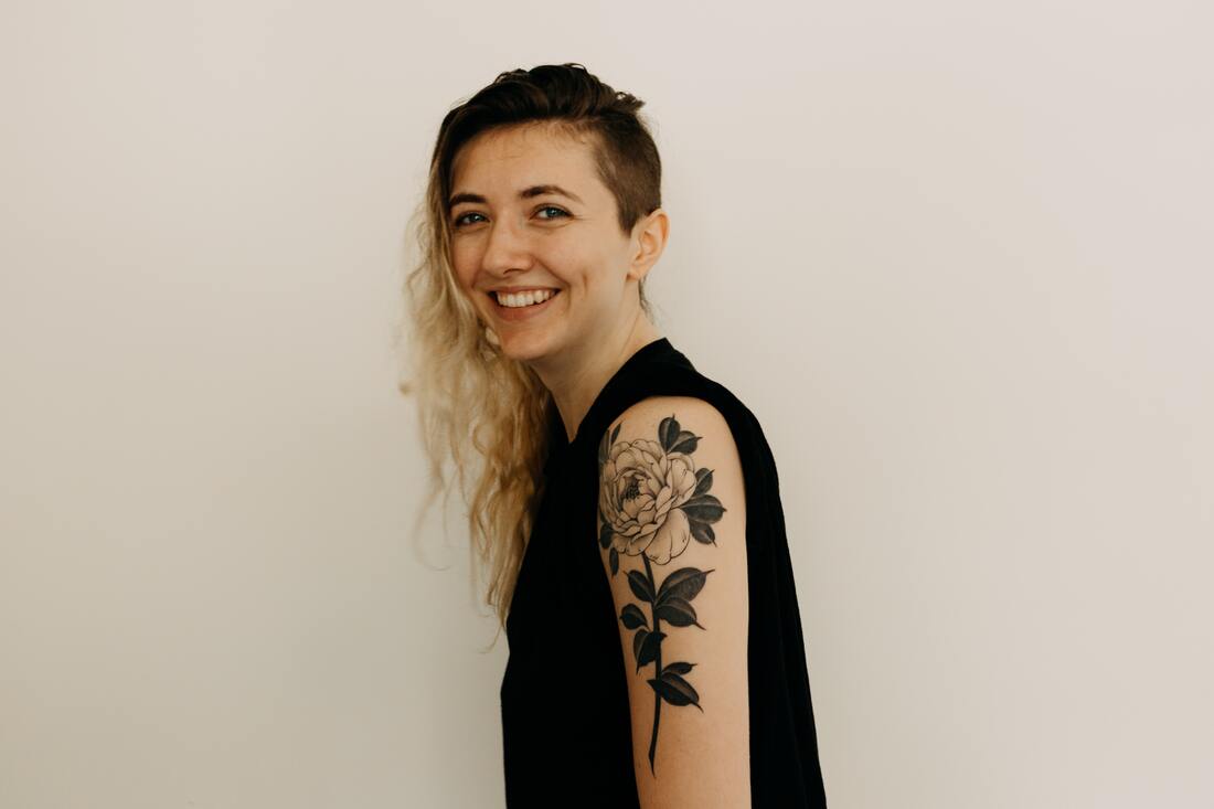 White woman with tattoo smiling at the camera. This represents that Sacred Circle Holistic Healing offers online counseling in Kansas for young adults who have low self-esteem and anxiety.