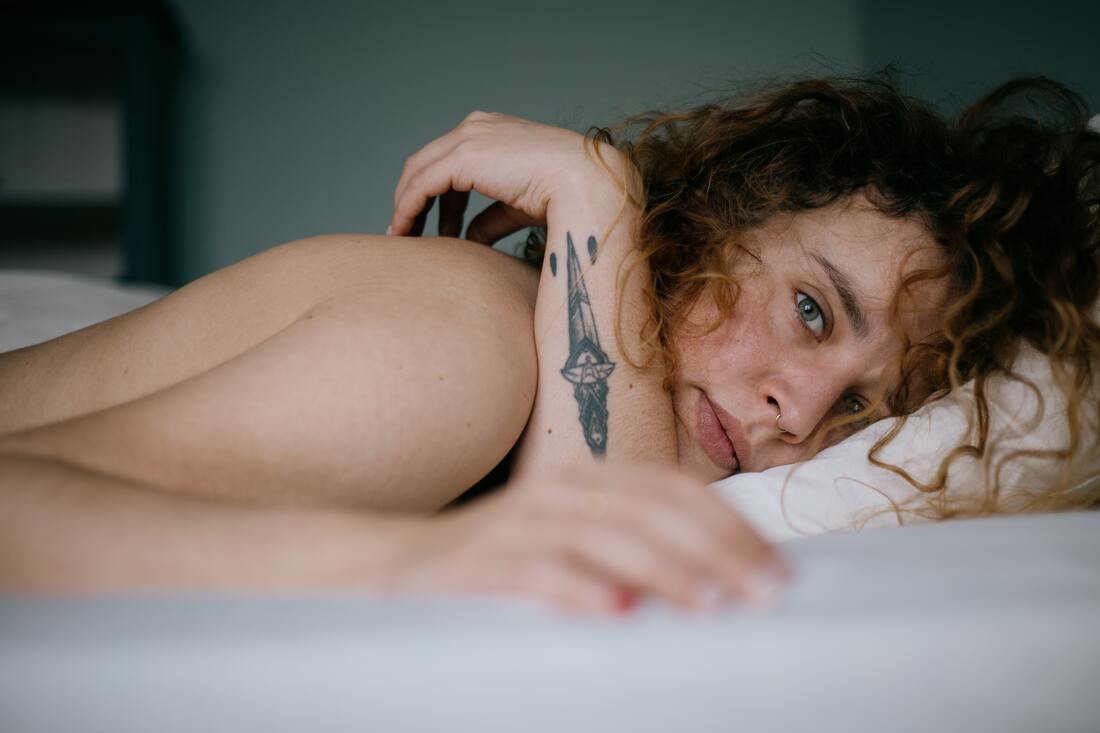 Young woman lying in bed, looking at the camera. This represents that Sacred Circle Holistic Healing offers online therapy in Kansas for young adults.
