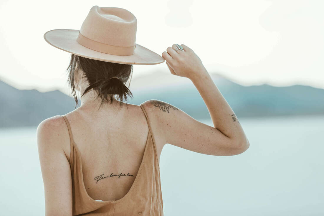 Back of a woman with one hand up, touching her hat and looking off into a natural landscape. This represents the introspection and self-understanding that happens through Holistic Life Coaching.